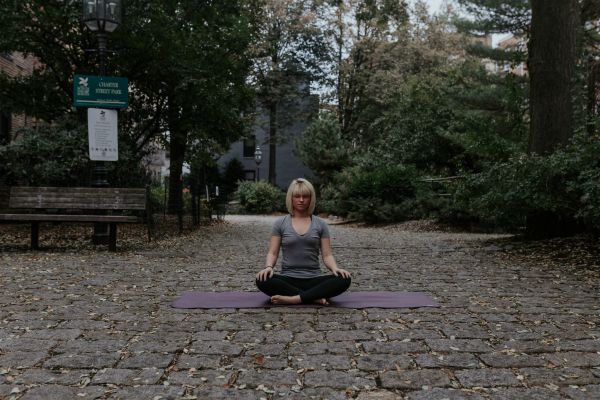 Woman sitting cross legged outside doing yoga | 11 Beginner-Approved Yoga Exercises to Boost Your Day