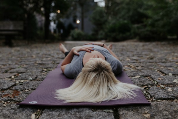 Woman doing yoga outside corpse pose | 11 Beginner-Approved Yoga Exercises to Boost Your Day