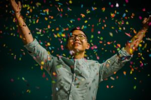 asian man throwing colorful confetti | Have a Happy Holiday by Sticking to Your Fitness Routine