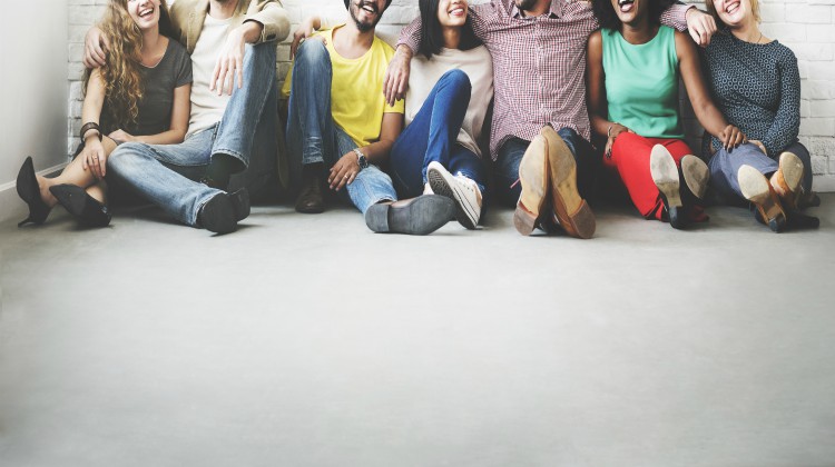 diverse friends sitting against wall laughing | The Science of Happiness: How to Focus on Friendship