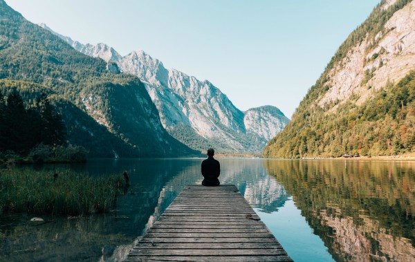silhouette man sitting on a dock against mountains | How to Define Mindfulness and 3 Ways to Try It