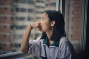 asian woman looking out window pensively | How to Define Gratitude and Use It in 2018