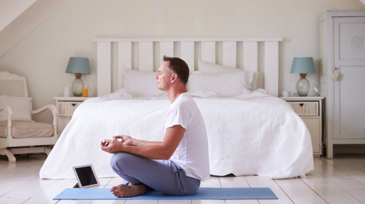 man sitting in room meditating with tablet | The Best Meditation Apps to Finally Destress in 2018 https://positiveroutines.com/best-meditation-apps-new-year/
