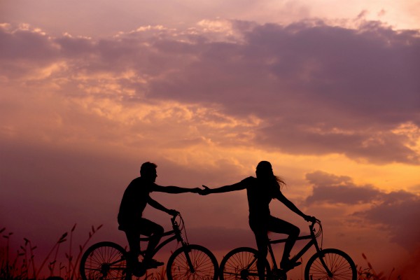 two silhouettes against sunset on bikes holding hands | Mindfulness for Anxiety Works. Here Are 2 Ways to Try it. https://positiveroutines.com/mindfulness-for-anxiety/ 