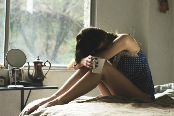 woman on bed with head on knees holding coffee | Why Sleep is Key to Increasing Productivity