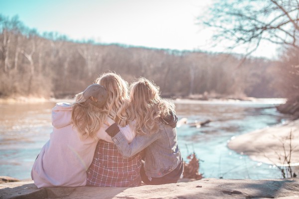 three blonds sitting overlooking river hugging | How to Be Happier This International Day of Happiness
