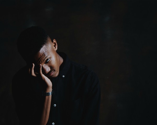 black man with head in hands looking unhappy | The Research-Backed Guide to Money and Happiness https://positiveroutines.com/money-and-happiness-guide/