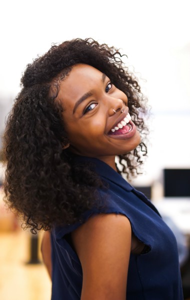 black woman smiling in an office | How to Be More Positive at Work, According to Science