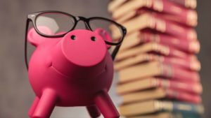 happy piggy bank with glasses near stack of books | The Research-Backed Guide to Money and Happiness