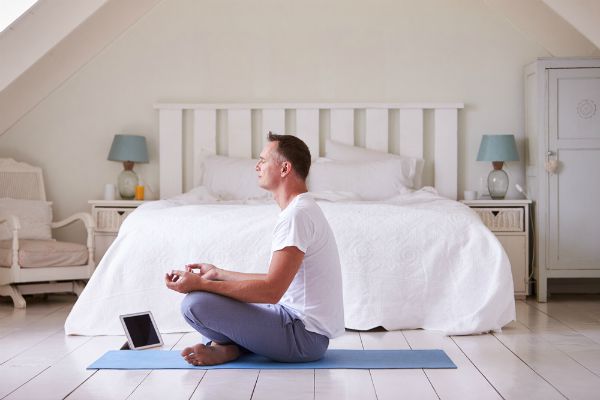 man meditating in bedroom with tablet | 26 Ways to Make Practicing Mindfulness Part of Your Day