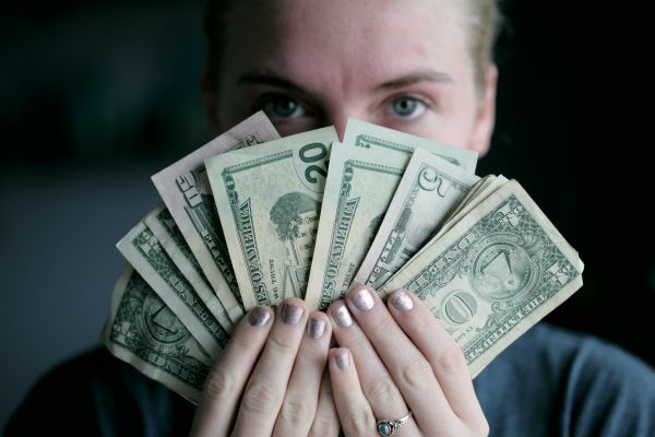 woman holding money fanned in front of face | The Research-Backed Guide to Money and Happiness