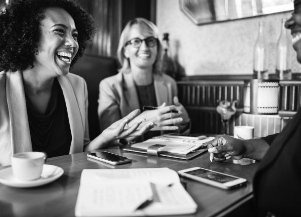 black and white businesswomen laughing at table | Feeling Work Stress? 1 Surprising Way to Get Relief https://positiveroutines.com/work-stress-relief/