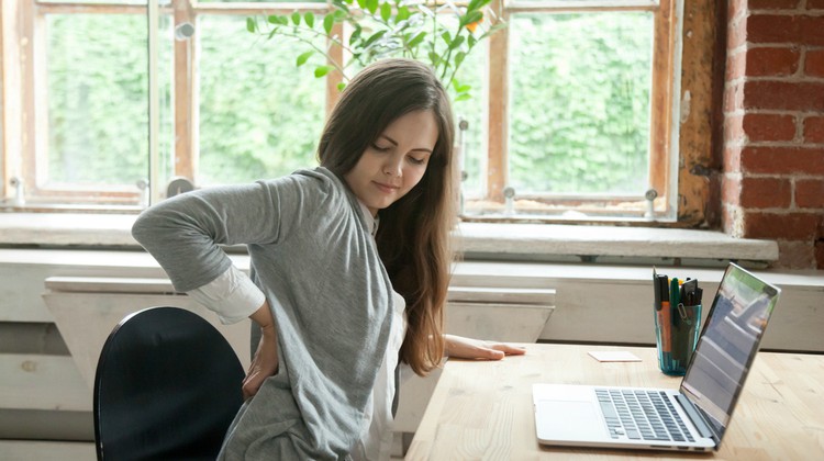 businesswoman working at desk back pain | The Best Hip Exercises for People Who Sit All Day https://positiveroutines.com/best-hip-exercises/
