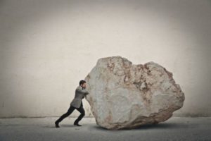 businessman pushing giant rock | 72 Resources to Overcome Procrastination and Improve Productivity https://positiveroutines.com/overcome-procrastination-resources/