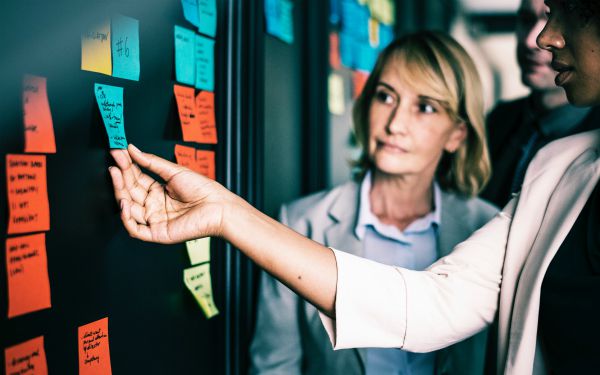 businesswomen moving sticky notes in office | Feeling Work Stress? 1 Surprising Way to Get Relief https://positiveroutines.com/work-stress-relief/