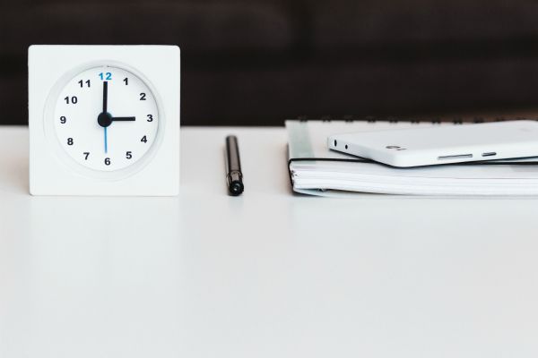 white clock pen and notebook on white table | How to Improve Productivity in the Workplace and Beyond