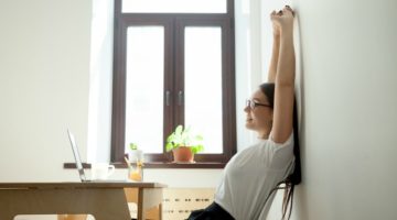 woman at desk stretching arms taking a break | Feeling Work Stress? 1 Surprising Way to Get Relief https://positiveroutines.com/work-stress-relief/
