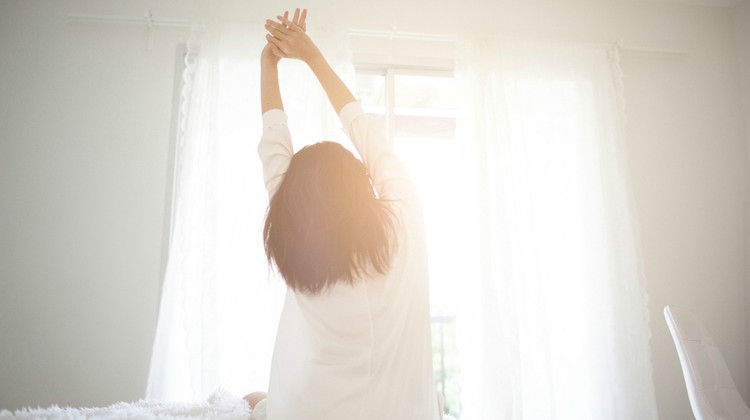 woman stretching in front of window in bed morning | An Adult Bedtime Routine for the Best Sleep Ever https://positiveroutines.com/bedtime-routine-for-adults/