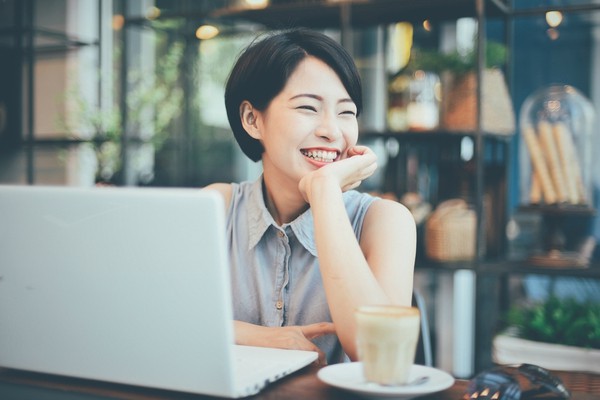 Asian woman smiling at laptop | Can Staying Positive Increase Your Productivity? https://positiveroutines.com/staying-positive-increase-productivity/