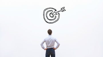 man standing and facing bullseye on wall | What are SMART Goals + How Do You Set Them? https://positiveroutines.com/what-are-smart-goals/