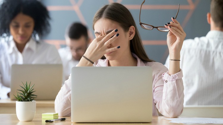 tired business woman at laptop rubbing forehead | Expert Advice on Being Productive in Tough Times https://positiveroutines.com/being-productive-in-tough-times/