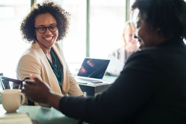 woman smiling as coworker shows her something | Can Staying Positive Increase Your Productivity? https://positiveroutines.com/staying-positive-increase-productivity/