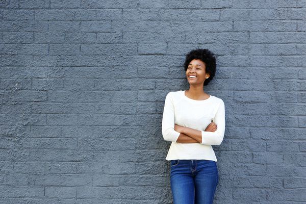 woman standing against wall looking away happy | Why You Need to Try Loving-Kindness Meditation https://positiveroutines.com/loving-kindness-meditation/