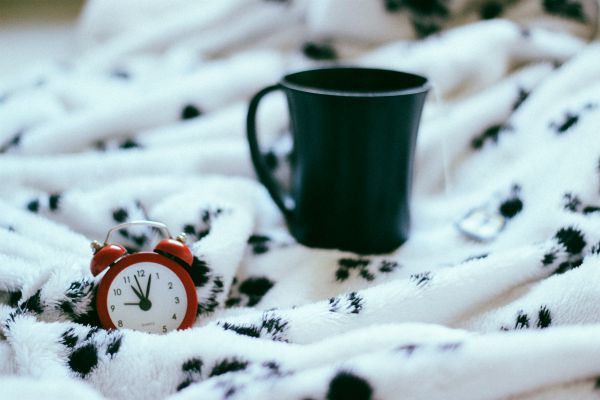 cup of tea on bed with red alarm clock | One of the Best Benefits of Napping? Increased Productivity https://positiveroutines.com/productivity-benefits-of-napping/