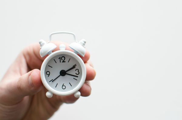 hand holding tiny white alarm clock | One of the Best Benefits of Napping? Increased Productivity https://positiveroutines.com/productivity-benefits-of-napping/