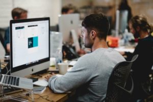 man working on computer in open office | One of the Best Benefits of Napping? Increased Productivity https://positiveroutines.com/productivity-benefits-of-napping/