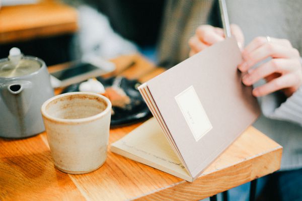 woman writing in open journal on wooden table | The Best Decluttering Tips for a Productive Workspace https://positiveroutines.com/decluttering-tips/