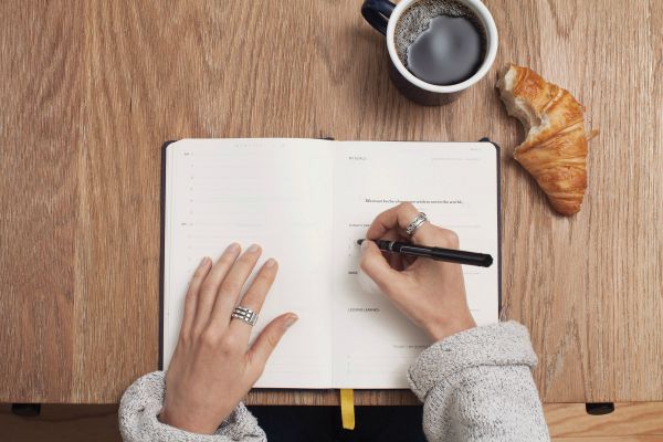 woman writing in planner on wooden desk | 5 Surprising Habits of Super Productive People