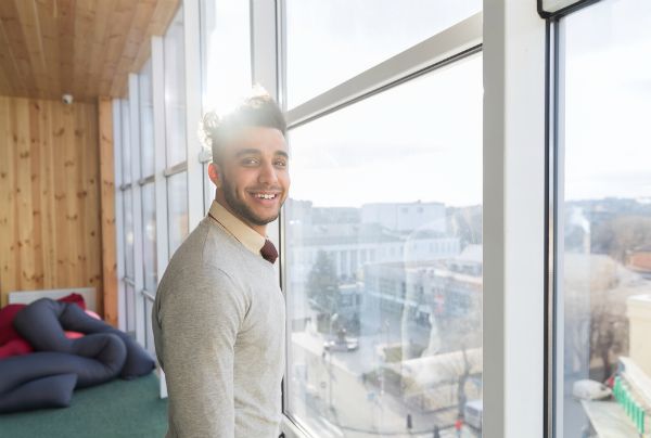 young businessman smiling in sunlight looking out office window | 59 Work Tips to Be Better At Your Job  https://positiveroutines.com/best-work-tips/