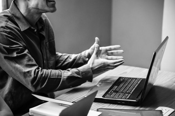 black and white of man animatedly talking at laptop | How to Handle Job Burnout, Even If You Love Your Work https://positiveroutines.com/job-burnout-guide/