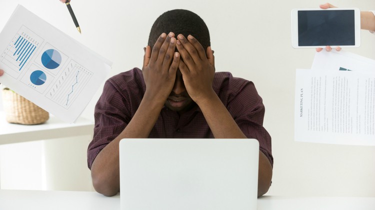 black man with head in hands in front of laptop | How to Handle Job Burnout, Even If You Love Your Work https://positiveroutines.com/job-burnout-guide/