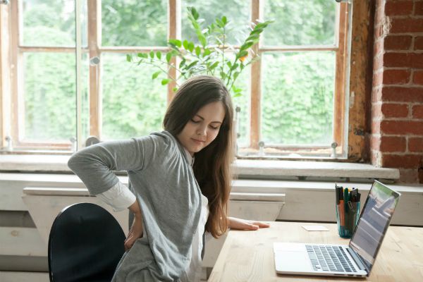 business woman holding her back in pain at work | How to Handle Job Burnout, Even If You Love Your Work https://positiveroutines.com/job-burnout-guide/