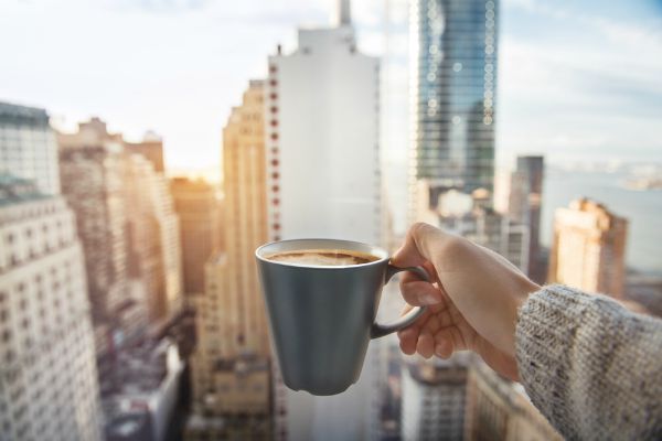 hand holding cup of coffee against city skyline | Feeling stressed out? 46 Ways to Take Control Now https://positiveroutines.com/tips-for-feeling-stressed/