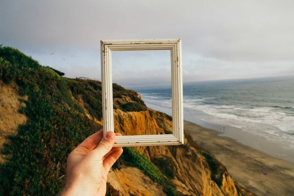 hand holding frame against ocean and cliffs | Why is Finding Meaning In Life and Work So Important? https://positiveroutines.com/finding-meaning/ 