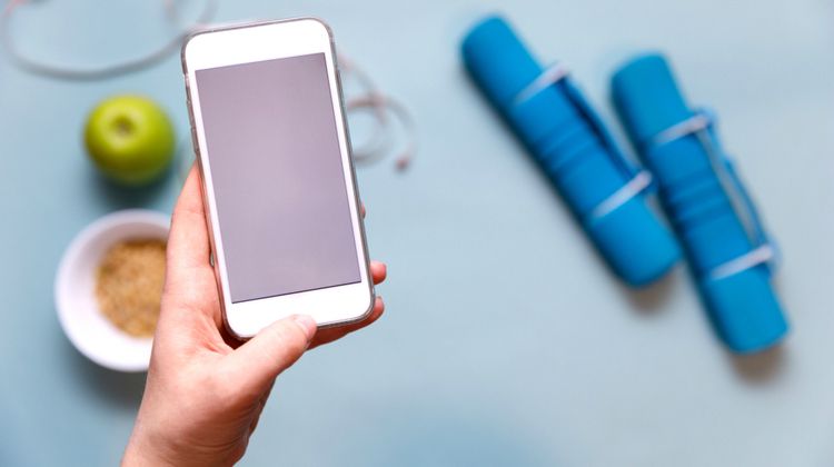 hand holding smartphone over background with apple and foam roller |The Best Habit-Tracking Apps for iPhone https://positiveroutines.com/best-habit-tracking-apps-iphone/