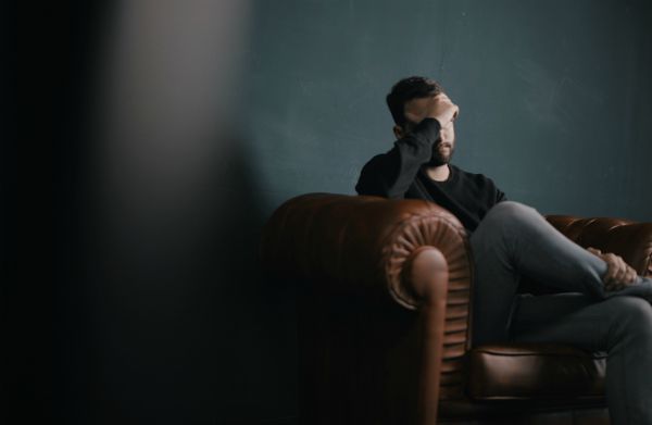 man sitting on couch holding forehead stressed | How to Handle Job Burnout, Even If You Love Your Work https://positiveroutines.com/job-burnout-guide/