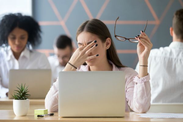 woman holding forehead in open office | How to Handle Job Burnout, Even If You Love Your Work https://positiveroutines.com/job-burnout-guide/