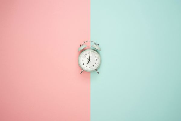 alarm clock against pink and teal split background | For Ultimate Productivity, Manage Your Energy, Not Your Time  https://positiveroutines.com/manage-your-energy-not-your-time/ 