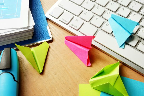folded up brightly colored paper airplanes on desk | 83 Secrets To Make You Happier At Work https://positiveroutines.com/happier-at-work/