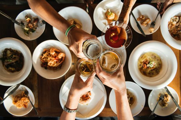 four people clinking glasses together over food | These 9 Positive Habits Will Make Your Life Better https://positiveroutines.com/positive-habits/