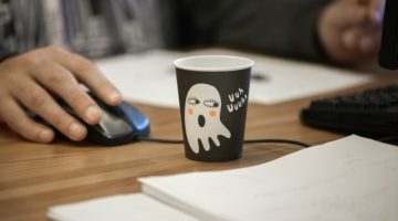 man working at laptop with halloween themed cup on desk | 11 Clever Halloween Costumes for the Productivity Obsessed  https://positiveroutines.com/clever-halloween-costumes/