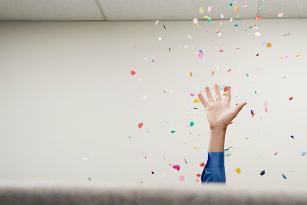 raised hand with confetti from cubicle | 83 Secrets To Make You Happier At Work https://positiveroutines.com/happier-at-work/