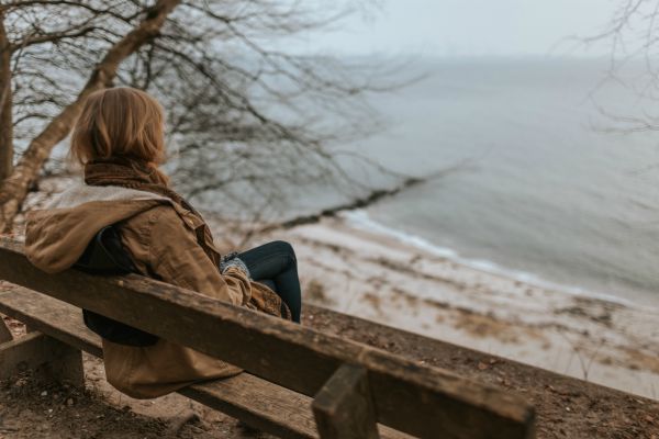 woman sitting on bench looking at ocean in winter | In Time for the Holidays: How to Take Breaks Effectively  https://positiveroutines.com/how-to-take-breaks/