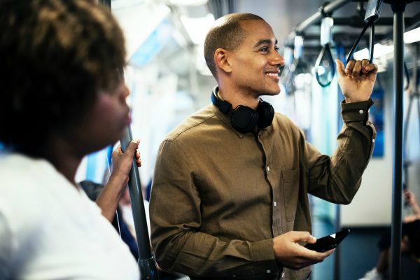 young man smiling holding phone on subway | How to Make the Most of Your Commute to Work https://positiveroutines.com/commute-to-work-tips/