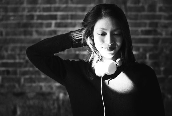 black and white image of woman smiling with headphones around neck | What Are Binaural Beats + Can They Boost Productivity? https://positiveroutines.com/what-are-binaural-beats/ ‎