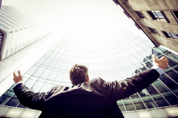 business man with arms outstretched looking up at city | 7 Surprising Ways to Be Successful at Work https://positiveroutines.com/successful-at-work/